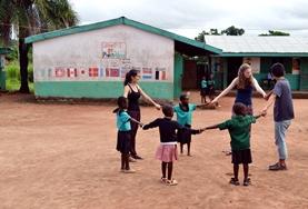 Care 19+ Care & Community volunteers play a game with children outside the classroom in Ghana.