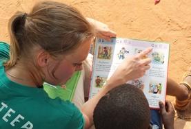 Togo A Care & Community with French Project High School Special volunteer reads to a young boy in Togo.