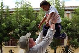 Volunteer Plays with Kids at a Kindergarten Abroad Volunteer throws girl up in the air while playing at a care center abroad
